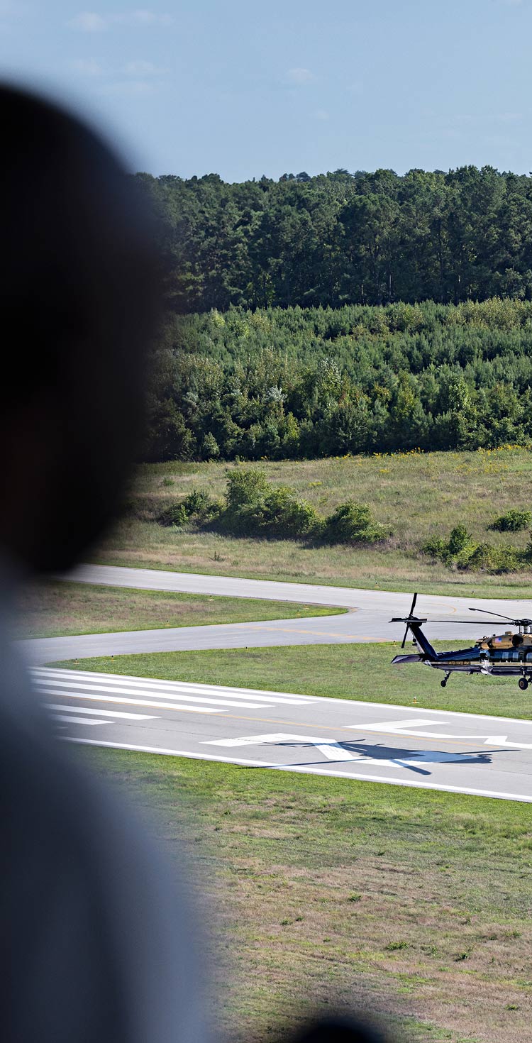 A man looking out a window at a helicopter landing on an airport runway