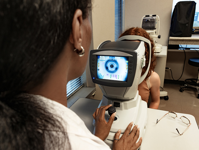 An optometric technician using a tonometer machine to perform an air puff test on a patient