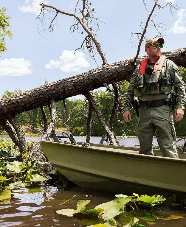 A male Conservation Officer standing on a boat on a lake next to a fallen tree