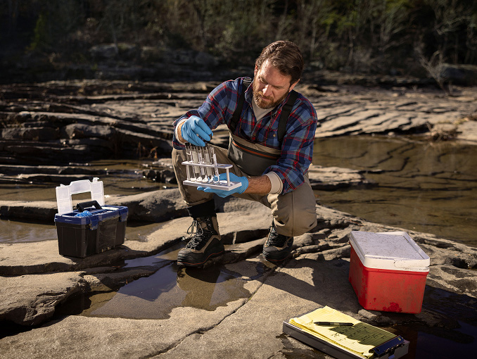 A man collecting samples of river water in test tubes in a forest preserve