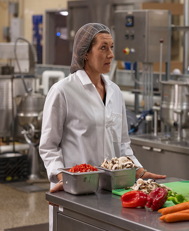 A female food tech standing in front of a prep table with sliced vegetables