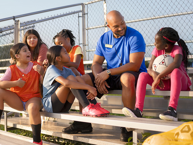 A male soccer coach sitting on bleachers with a group of children