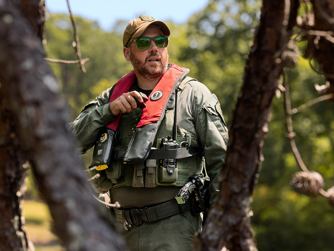 A conservation officer in a forest wearing a vest and sunglasses